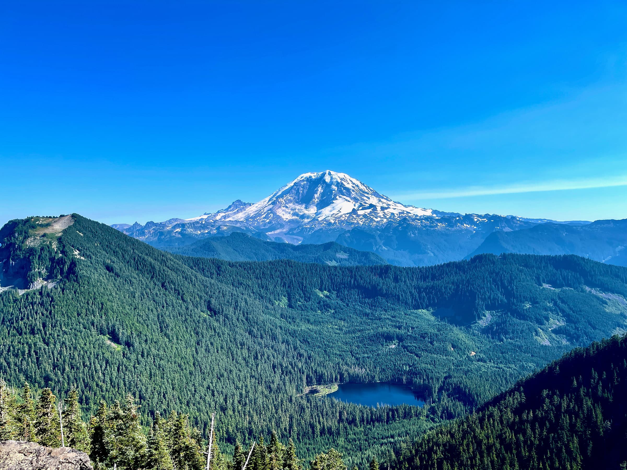 Mount Rainier above the forested ridges and a small alpine lake in the Cascades